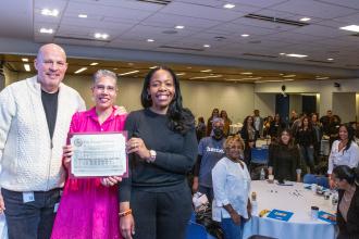 Michael Mulgrew, Rosemarie Thompson and Rita Joseph stand at the stage with members in the background