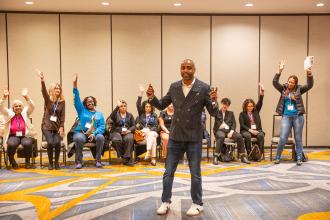 A man leading a workshop asks participants to raise their hands. 