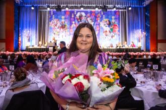 A woman smiles for the camera holding flowers after receiving an award. 