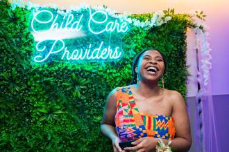 A woman laughs and smiles in front of a sign