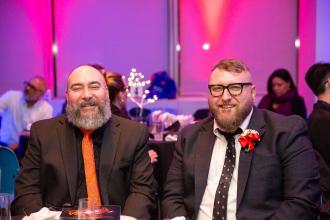 Two men sitting at a table smile for a photo.