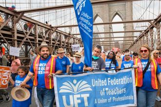 A group of men, women and children march over the Brooklyn Bridge with signs