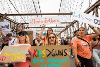 Members walking across the Brooklyn Bridge hold their signs in the air