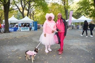 Two UFT members at the Manhattan Making Strides Walk on Oct. 20, 2024 smile for a photo while walking along with one of their dogs. 
