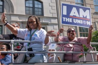 A group of members look down from the second deck of a double-decker bus at the 2022 Labor Day Parade 
