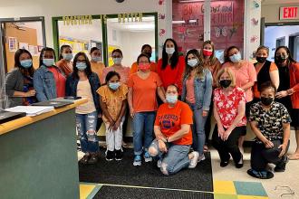 A group of staff members pose together wearing orange