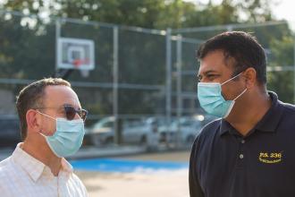 Two men wearing masks engage in conversation from a relatively close distance. 