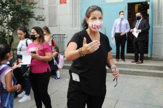 A woman wearing a mask with the words "love" directs students into a building.