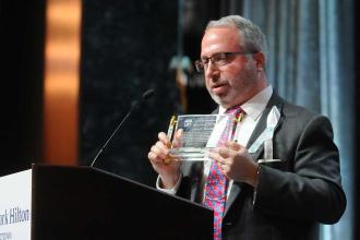 A man looks down while speaking to a crowd and holding an award. 