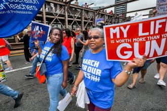 Two women walk across a bridge holding signs with a group