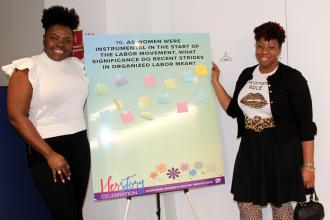 Two women pose next to a poster 