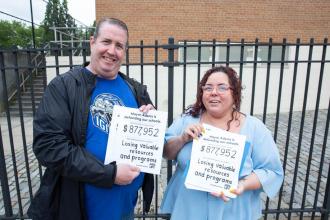 A man and woman hold signs and smile