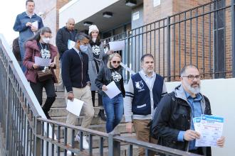 A group of staff members walk down the stairs outside of their school building