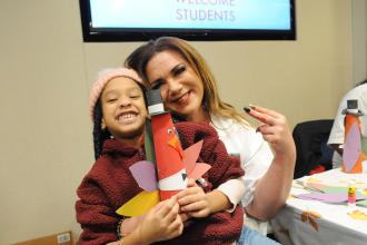 A woman and student pose for a photo showing off a paper turkey