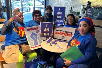 A group of members pose at a table holding their signs for the day of action