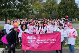 A large group of marchers take a photo with a pink banner in front of them