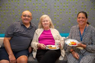 Three people smile for a photo while eating breakfast.