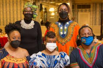 5 people all wearing masks pose for a group photo at a table. 