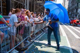 A man walking in the parade greets people cheering by the sidewalk. 