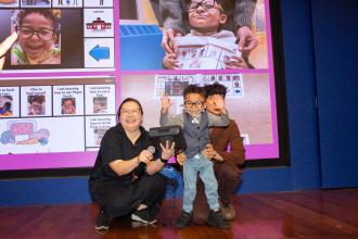 Speech teacher Georgia Duan of PS 347, the American Sign Language & English Lower School, in Manhattan and her student Aydin accept an award for Aydin’s “Fun with Food” augmentative and alternative communication (AAC) social stories project, with Aydin using his AAC device to thank the chapter for the award at the UFT Speech Improvement Chapter Better Speech and Hearing Month Celebration. 