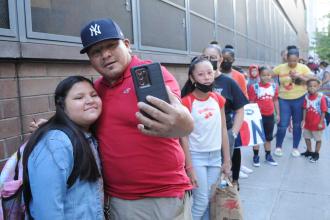 A father and daughter take a selfie outside a school