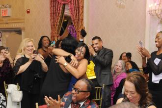 Teacher Jamila Reid (back to camera) is congratulated by her colleagues from PS 68 in the Bronx after she receives a Seasoned Teacher Award at the UFT District 11 Scholarship Dinner on March 28, 2025. 