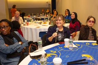 A woman smiles at a table while holding a microphone during the UFT Muslim Educators Committee on March 7, 2025. 