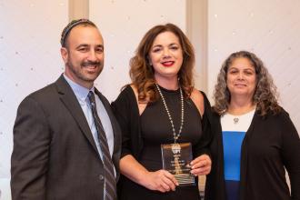 Three UFT members pose for a photo with the woman in the center holding an award she received at the UFT Jewish Heritage Committee's Tikkun Olam Awards Dinner on Dec. 5, 2024