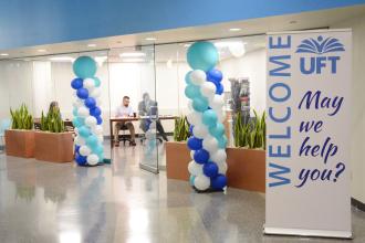 Open glass door flanked by two balloon columns and a banner that reads UFT: Welcome: May we help you?