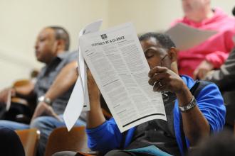 Man sitting in auditorium reading UFT contract on long sheet of paper