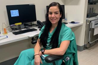 Nurse wearing green scrubs sits at desk in front of a computer
