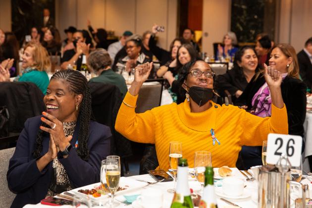 A woman on the right raises her hands in satisfaction and the women on the left claps and looks to her right.