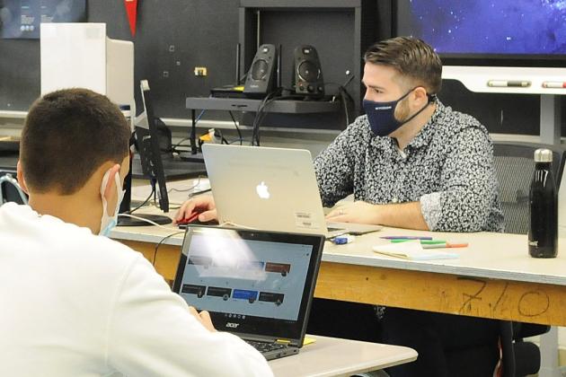 Three people sit at desks in a classroom all wearing masks 