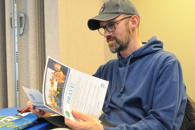 A man sits at a table and reads a pamphlet 