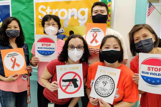 A group of staff members pose together wearing orange and holding signs 