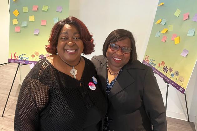 Two women pose for a photo while in a gallery