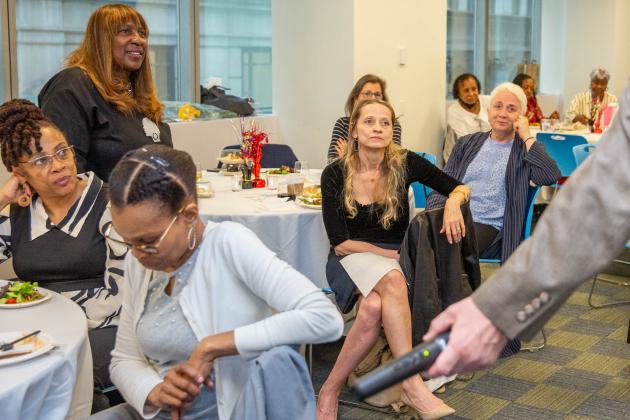 A group of attendees listen to a speaker while sitting at their tables