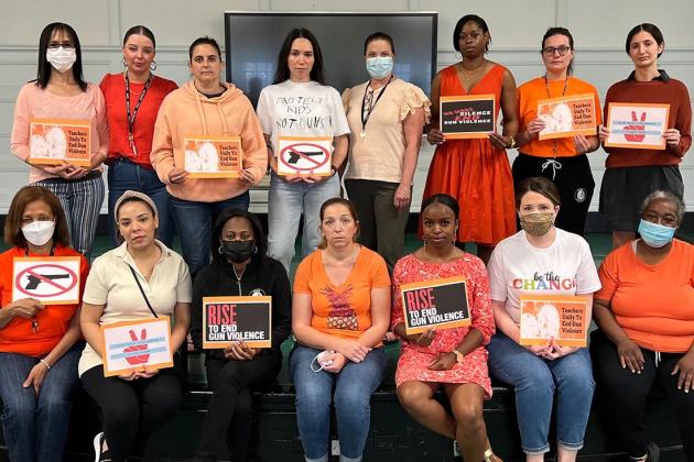 A group of staff members pose together wearing orange and holding signs 