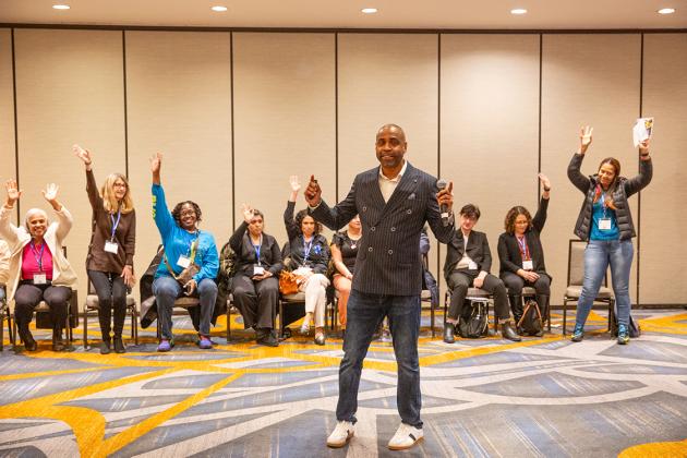 A man leading a workshop asks participants to raise their hands. 