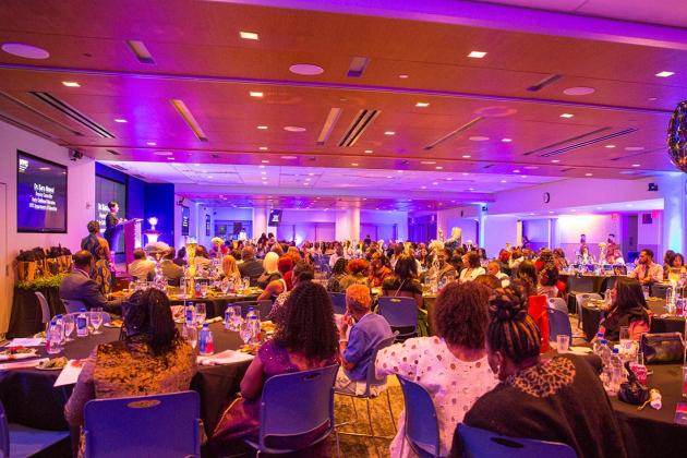 A large room is gathered with several tables full of guests 