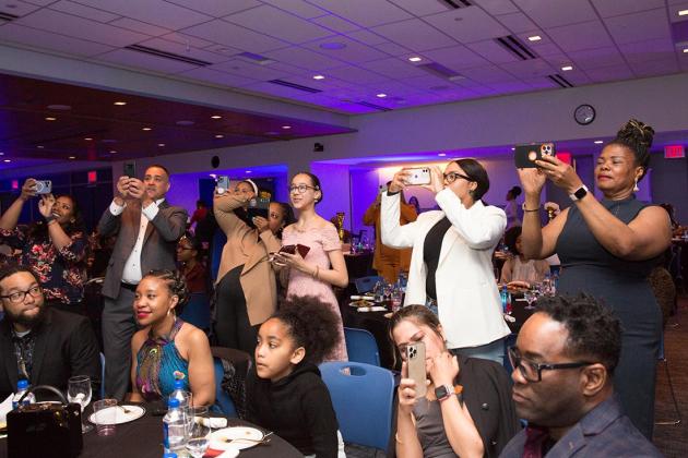 People in the crowd hold up their phones to record video and take pictures of the event 