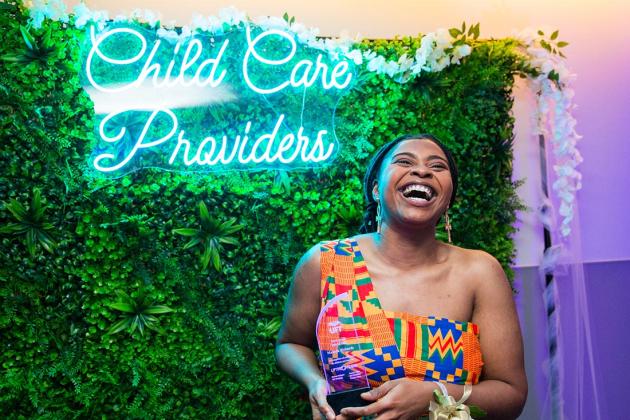 A woman laughs and smiles in front of a sign