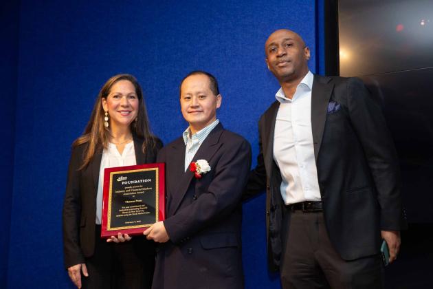 Three people pose for a photo - a woman on the left, man in the middle holding an award and a man on the right