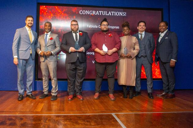A group of award winners pose for a photo on the stage. 