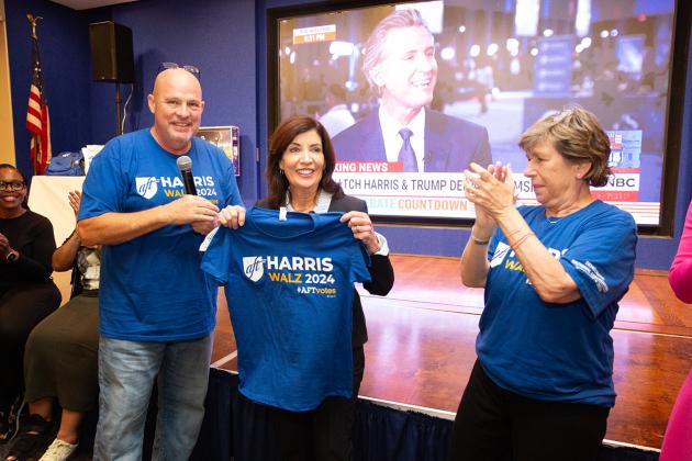 UFT President Michael Mulgrew presents Gov. Kathy Hochul with a T-shirt supporting the Harris-Walz ticket as AFT President Randi Weingarten looks on.