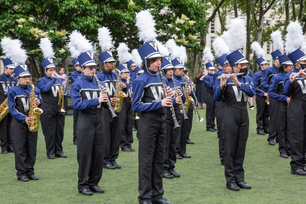 A marching band practices in a park before marching