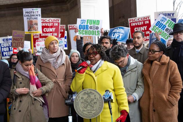 A woman speaks with a large crowd behind her showing support
