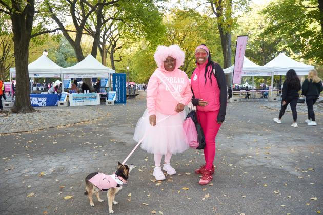 Two UFT members at the Manhattan Making Strides Walk on Oct. 20, 2024 smile for a photo while walking along with one of their dogs. 