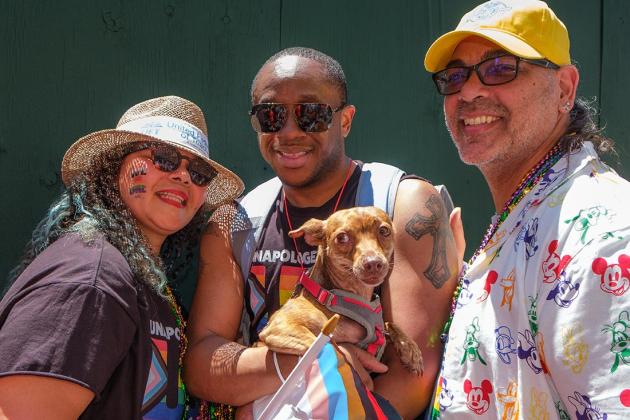 Three people pose while holding a dog 
