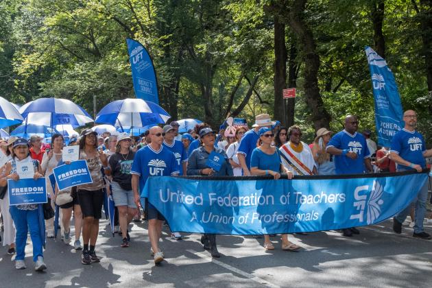 A group of union members march through a park surrounded by trees 